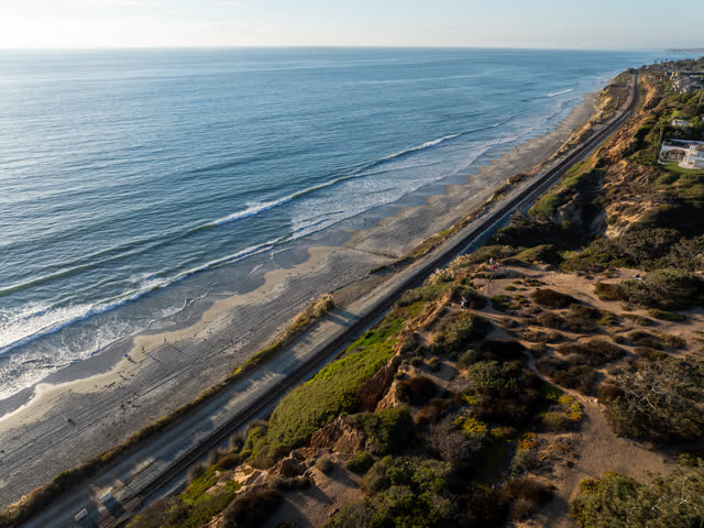 Aerial view of the cliffs, the surf and the ocean in Del Mar, with people walking.