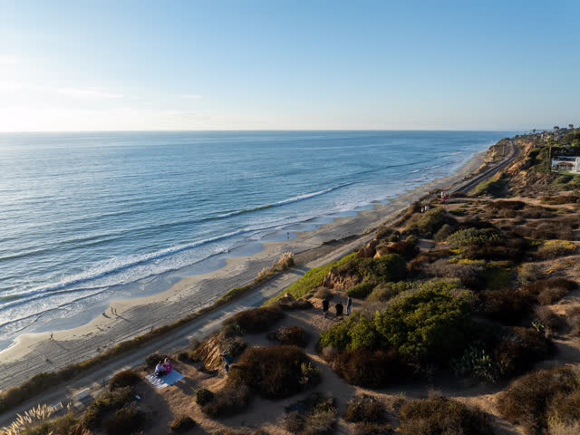 Aerial view of the cliffs, the surf and the ocean in Del Mar, with people walking.