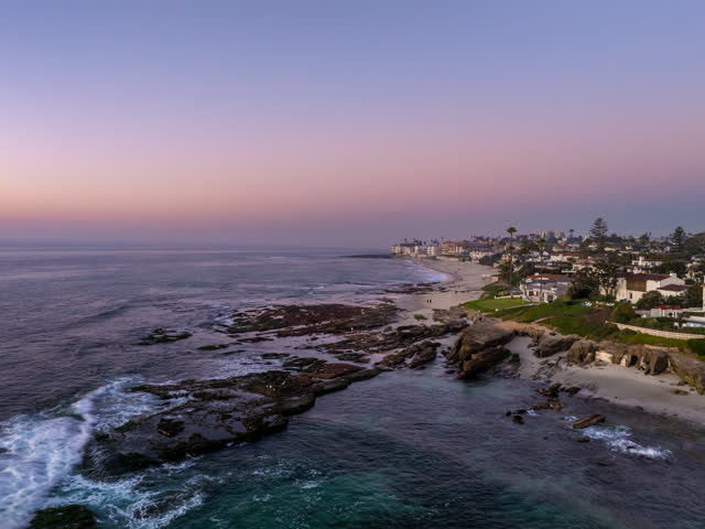 Aerial view of the cliffs, palm trees and the ocean at Windansea, with people walking.