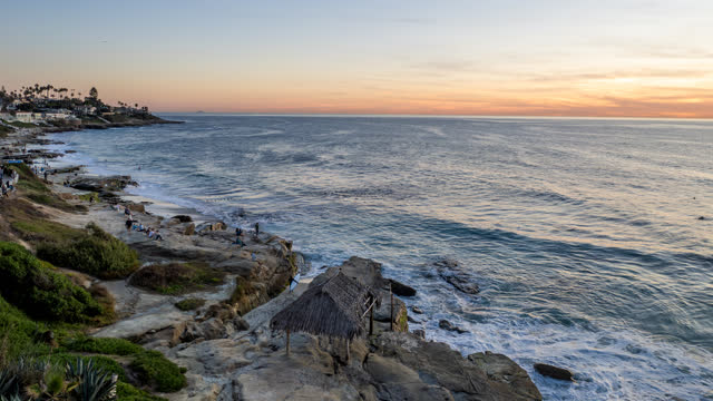 The cliffs, the surf and palm trees at Windansea, with people walking.