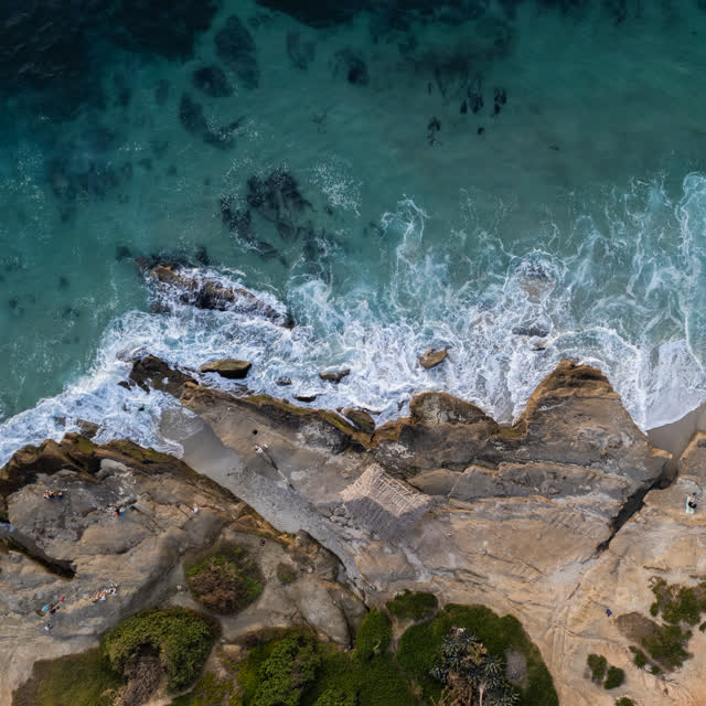 Aerial view of the cliffs, the surf and the ocean at Windansea, with people walking.