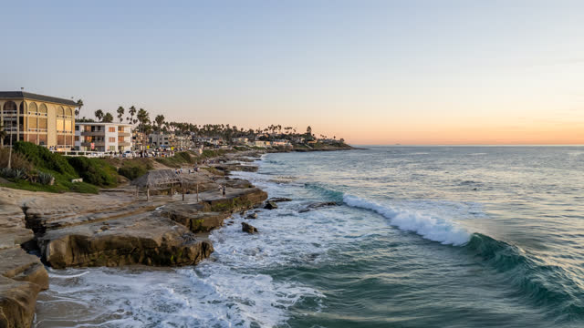 Low aerial view of the cliffs, the surf and palm trees at Windansea.