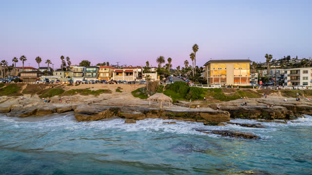 Low aerial view of the beach, palm trees and the ocean at Windansea, with people walking.