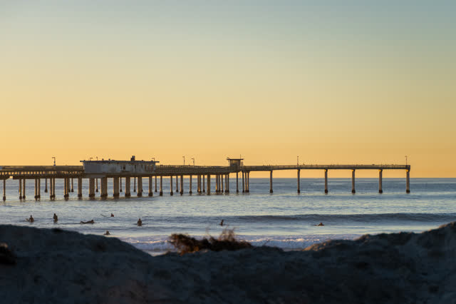 The beach, the surf and the pier in Ocean Beach, with surfers out.
