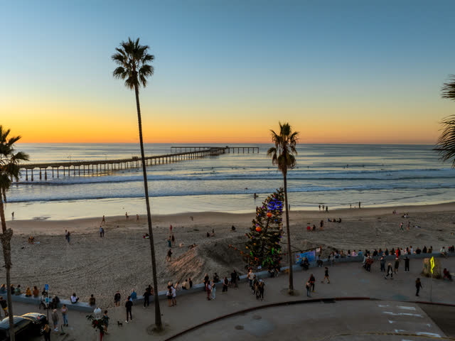 Elevated view of the beach, the surf and the pier in Ocean Beach, with a crowd gathered.