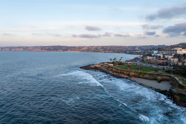 Aerial view of the cliffs, the surf and palm trees at La Jolla Cove, with people walking.