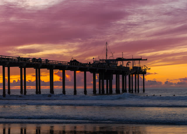 View from the water of the beach, the surf and the pier at La Jolla Shores, with surfers out.
