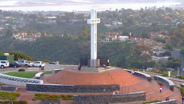 Low aerial view of a park, homes and traffic at Mount Soledad, with people walking.
