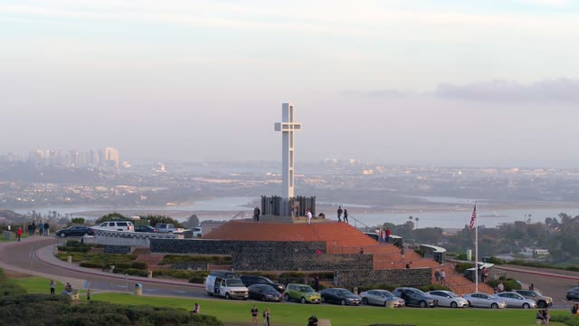 Low aerial view of a park, the skyline and the bay at Mount Soledad, with people walking.