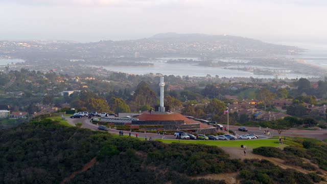 Low aerial view of the cliffs, the bay and homes at Mount Soledad, with people walking.