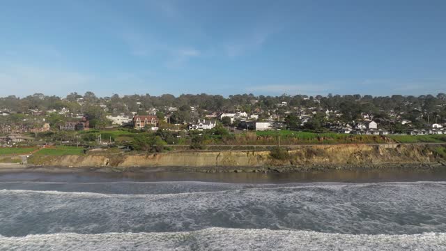 Low aerial view of the cliffs, the surf and the ocean in Del Mar.