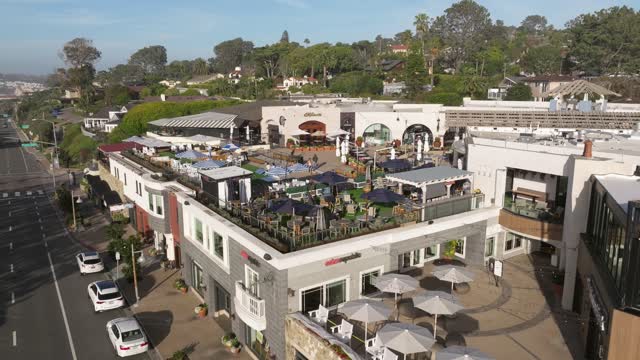 Low aerial view of the downtown streets, palm trees and the buildings in Del Mar, with people eating outside.