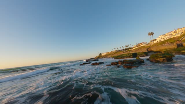 Low aerial view of the cliffs, the surf and palm trees at Windansea.
