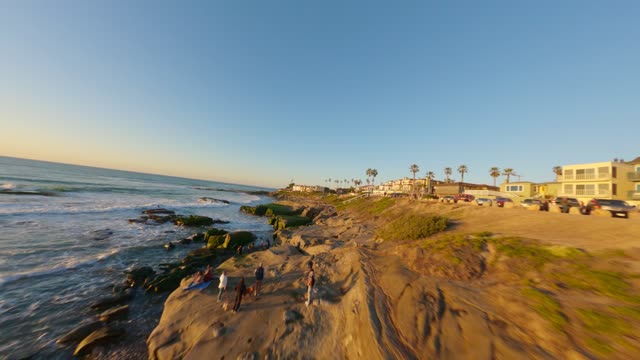 Low aerial view of the cliffs, the surf and palm trees at Windansea, with people walking.
