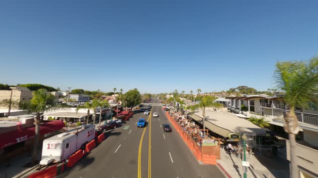 Low aerial view of the downtown streets, palm trees and homes at Downtown Encinitas, with people eating outside.