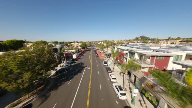 Low aerial view of the downtown streets, palm trees and homes at Downtown Encinitas, with people walking.