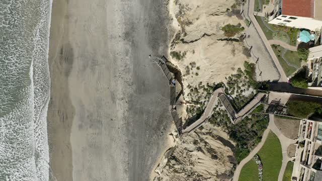 Aerial view of the cliffs, the surf and the ocean in Solana Beach, with people walking.