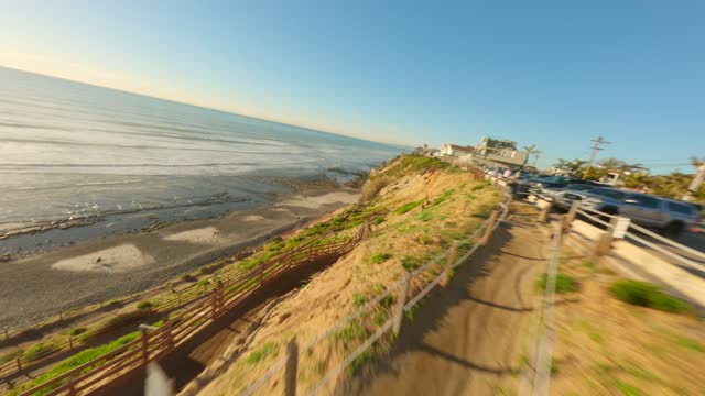 Low aerial view of the cliffs, the ocean and the beach at Leucadia, with people walking.