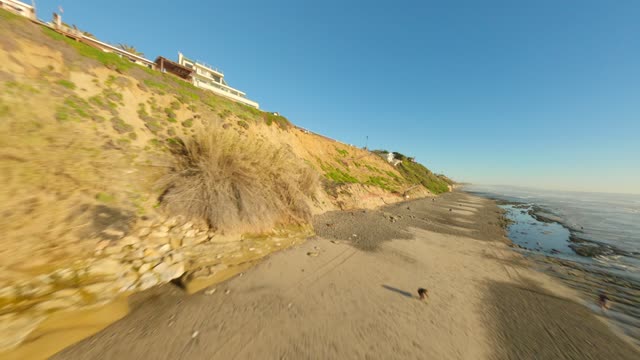 Low aerial view of the beach, the ocean and homes at Leucadia, with people walking.