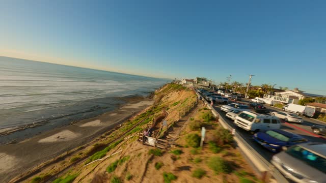 Low aerial view of the cliffs, the ocean and homes at Leucadia, with people walking.