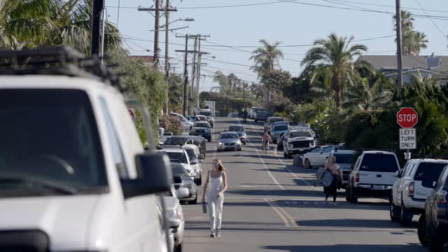 A residential street, palm trees and homes at Leucadia, with people walking.