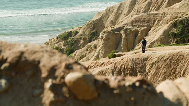 Elevated view of the cliffs, the surf and the ocean at Black’s Beach, with people walking.