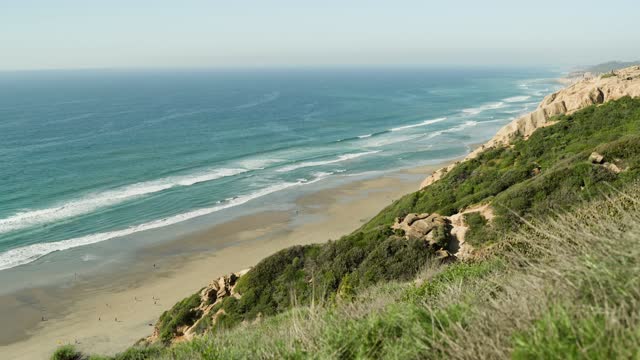 Elevated view of the cliffs, the surf and the ocean at Black’s Beach, with people walking.