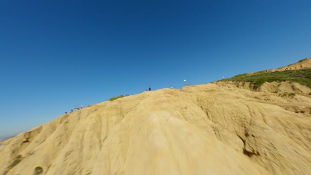 Low aerial view of the cliffs and open country at Black’s Beach, with people walking.