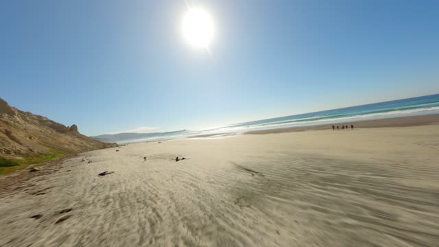 Low aerial view of the beach, the surf and the ocean at Black’s Beach, with people walking.