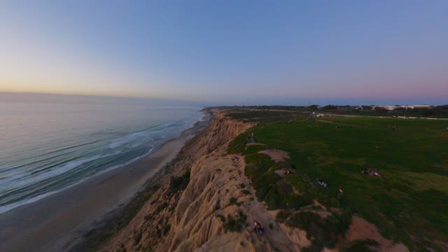 Aerial view of the cliffs, the ocean and the beach at Black’s Beach, with people walking.