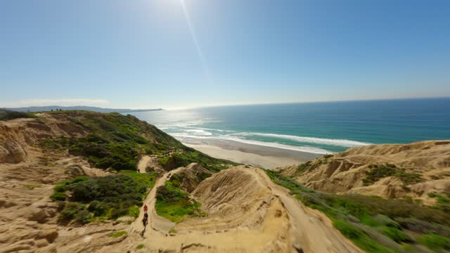 Low aerial view of the cliffs, the surf and the ocean at Black’s Beach, with people walking.