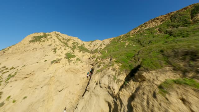 Low aerial view of the cliffs and open country at Black’s Beach, with people walking.