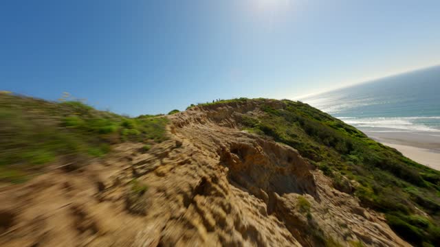 Low aerial view of the cliffs, the ocean and the beach at Black’s Beach, with people walking.