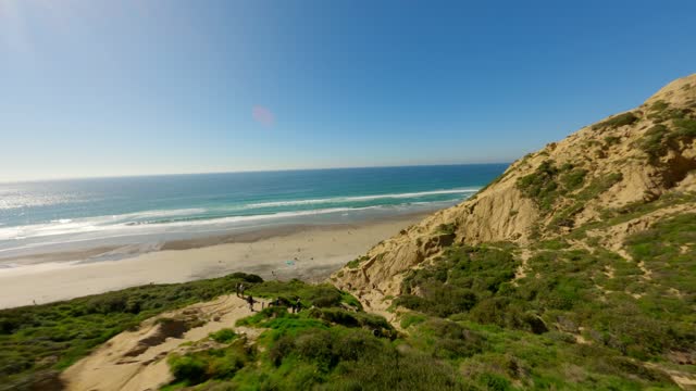 Elevated view of the cliffs, the surf and the ocean at Black’s Beach, with people walking.