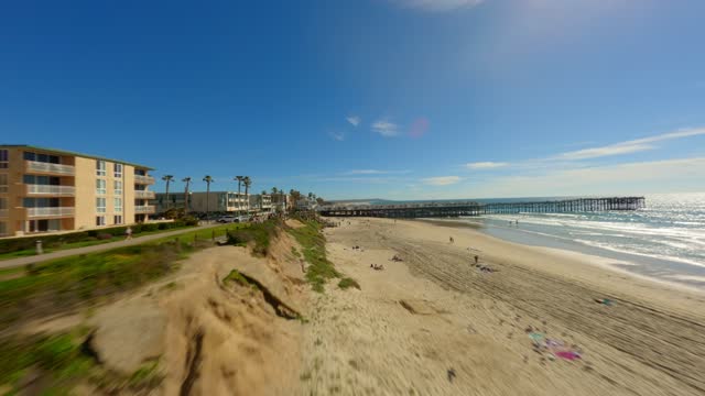 Low aerial view of the beach, the surf and the pier in Pacific Beach, with people walking.