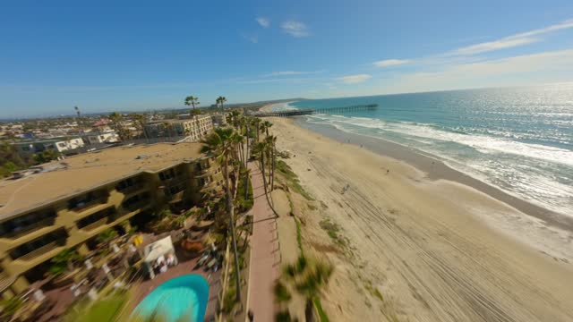 Low aerial view of the beach, the surf and the pier in Pacific Beach, with people walking.
