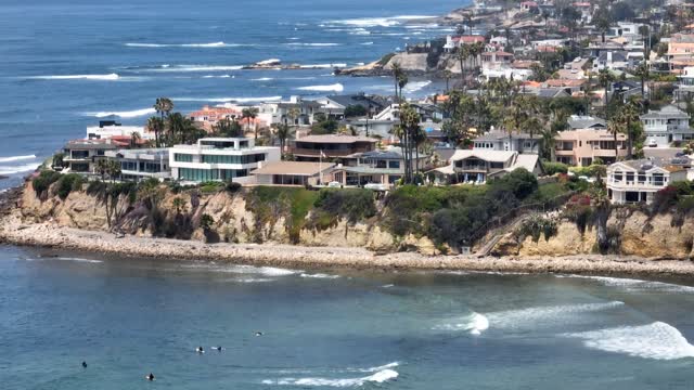 Aerial view of the cliffs, the surf and palm trees in Pacific Beach, with surfers out.