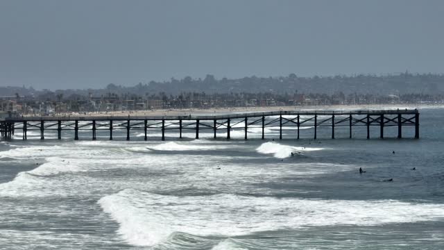Low aerial view of the beach, the surf and the pier in Pacific Beach, with surfers out.