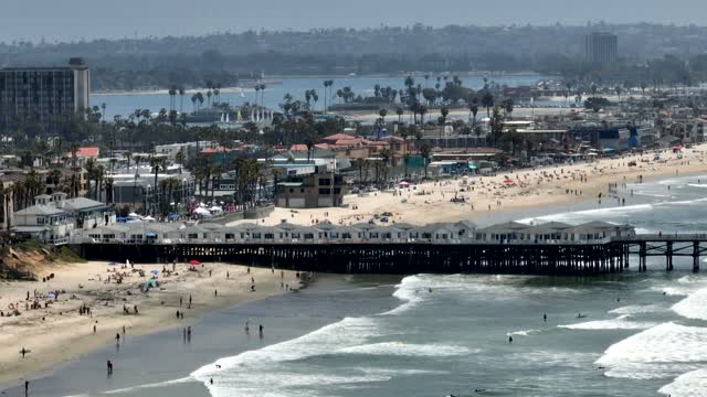 Aerial view of the beach, the surf and the pier in Pacific Beach, with people walking.