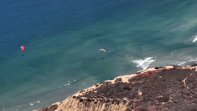 Aerial view of the cliffs, the surf and the ocean at Black’s Beach, with a crowd gathered.