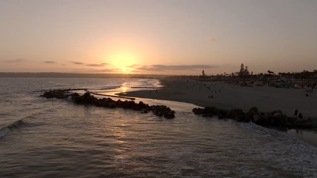 Low aerial view of the beach, the surf and palm trees at Coronado Beach, with people walking.