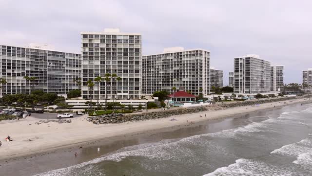 Low aerial view of the beach, the surf and palm trees at Coronado Beach, with people walking.