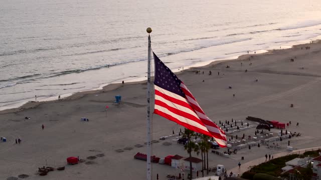 Low aerial view of the beach, the surf and palm trees at Coronado Beach, with people walking.