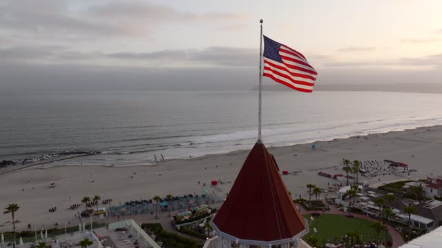 Low aerial view of the beach, palm trees and the ocean at Coronado Beach, with people walking.