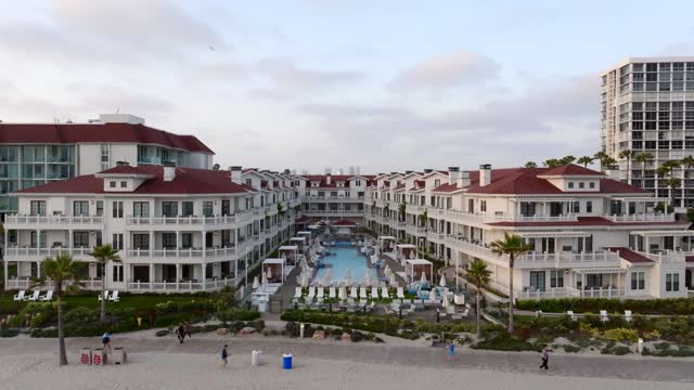 Low aerial view of the beach, palm trees and homes at Coronado Beach, with people walking.