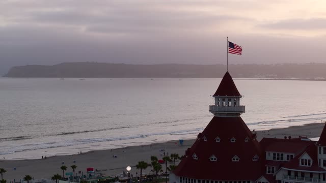 Low aerial view of the beach, palm trees and the ocean at Coronado Beach, with people walking.