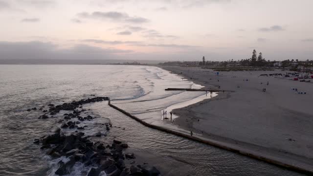 Low aerial view of the beach, the surf and palm trees at Coronado Beach, with people walking.