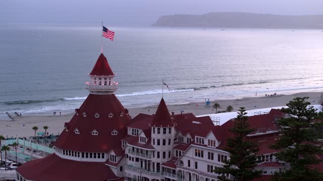 Low aerial view of the beach, palm trees and the ocean at Coronado Beach, with people walking.