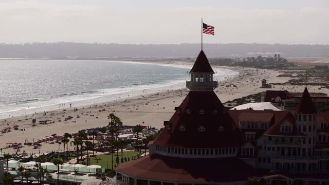 Low aerial view of the beach, palm trees and the ocean at Coronado Beach, with people walking.