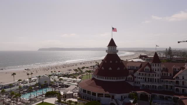 Low aerial view of the beach, palm trees and the ocean at Coronado Beach, with people walking.